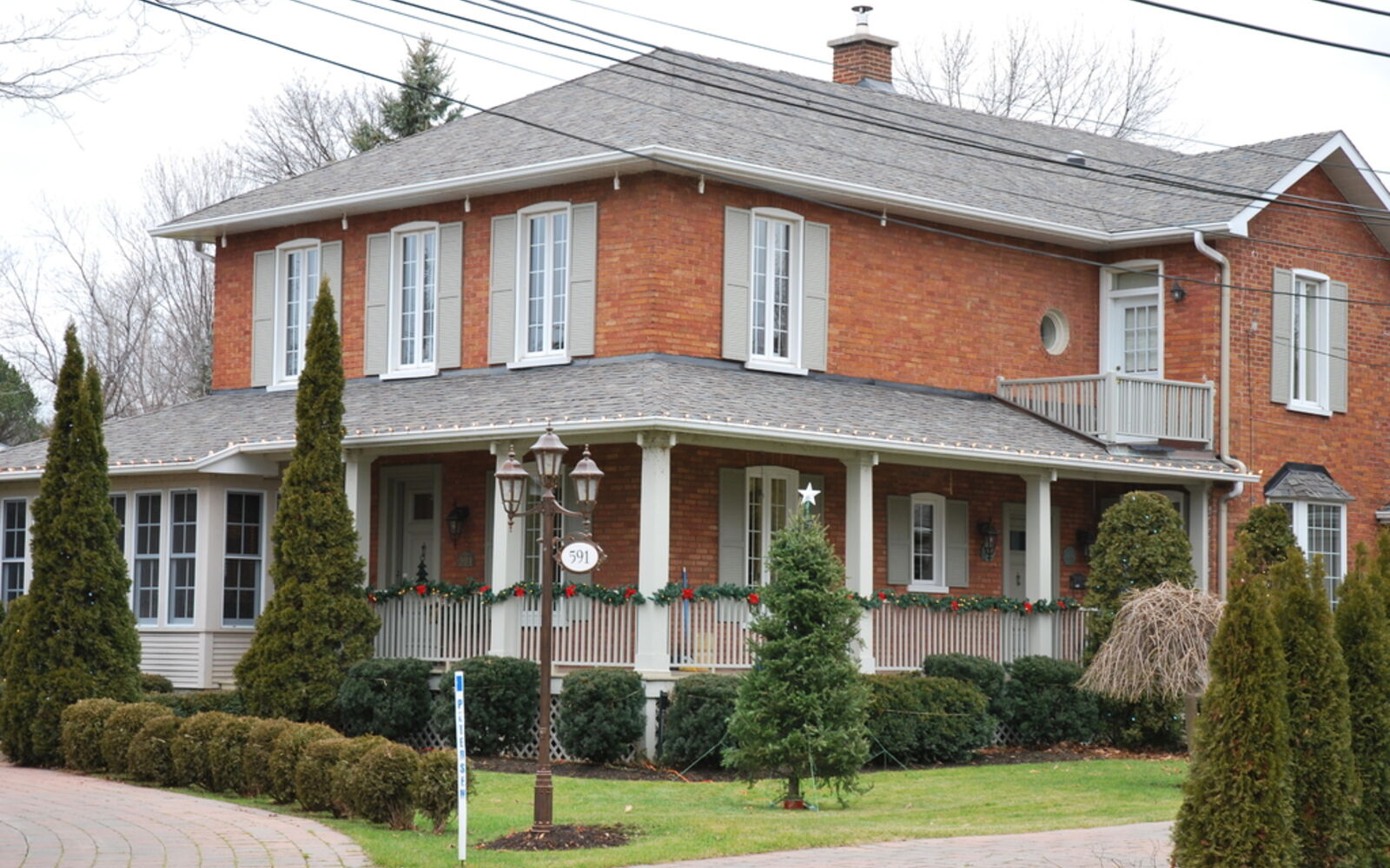 A red brick farmhouse with a wide covered porch, white trim and neatly trimmed evergreens