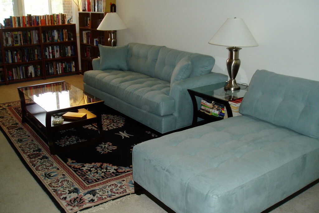 A bright living room with a pale blue sofa and chaise, a patterned rug and a dark wood coffee table