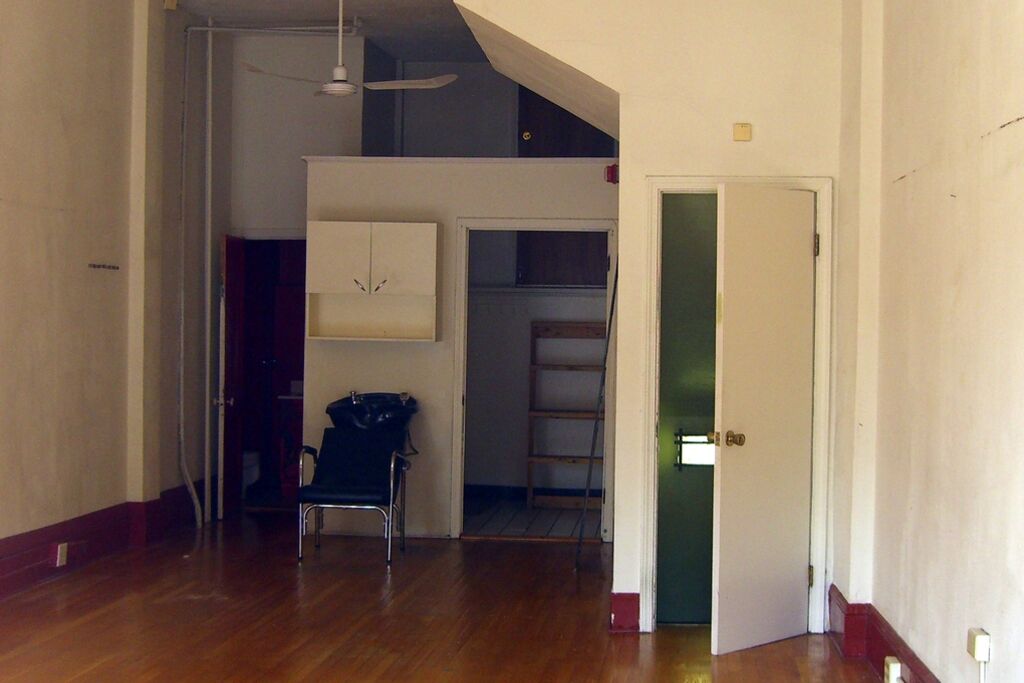 An open room with warm hardwood floors, white walls and a doorway to a back room